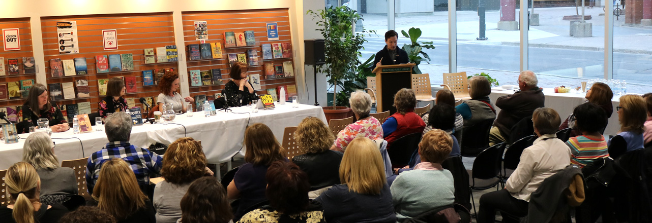 crowd in front of speaking panel in room with large windows