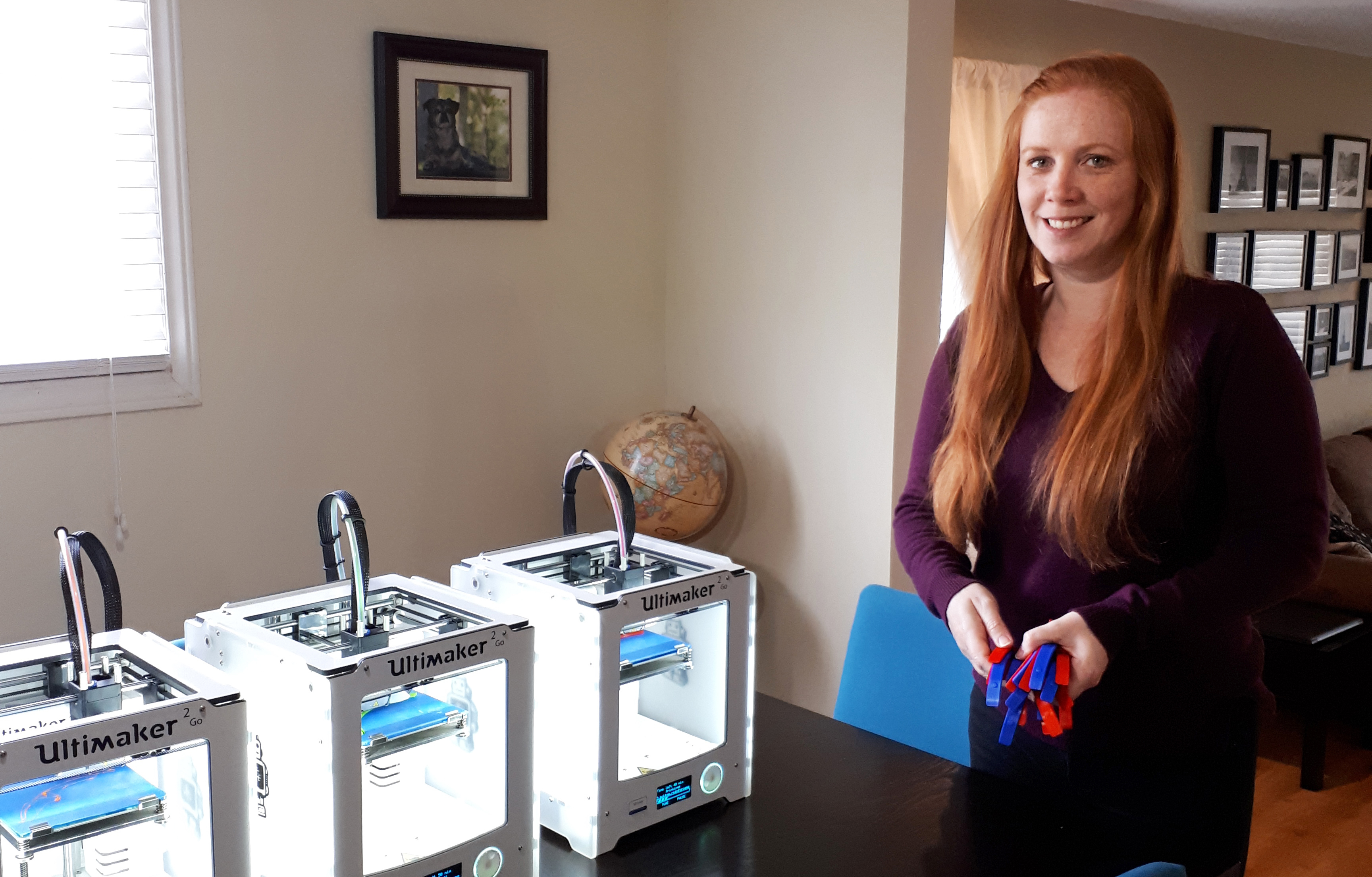 person standing next to 3d printers holding face shield parts