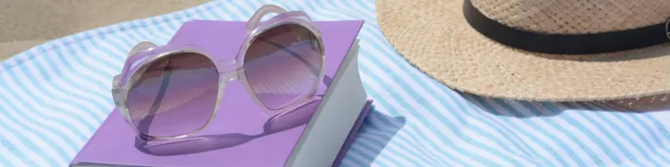 photo of a book, a pair of sunglasses, and a summer hat on a beach blanker